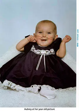 A baby in black dress with white lace around it's neck.