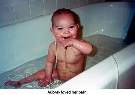 A baby sitting in the tub with his mouth open.